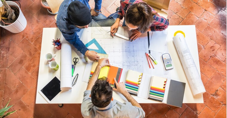 Three people looking at a blueprint and taking measurements