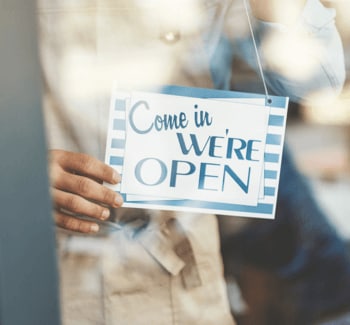 Worker hanging "Come in, We're Open" sign Worker hanging "Come in, We're Open" sign