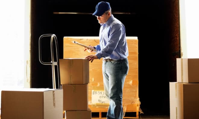 Man with clipboard looking at boxes next to a pallet Man with clipboard looking at boxes next to a pallet