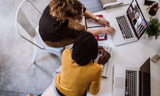 Two coworkers looking at laptop together Two coworkers looking at laptop together