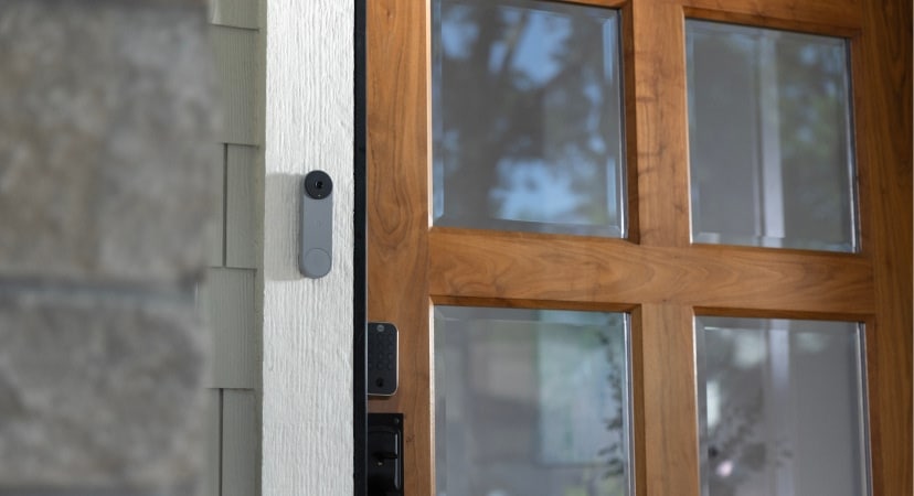 Close-up of a smart doorbell and electronic lock installed next to a wooden front door, illustrating key smart home security devices for new homeowners.