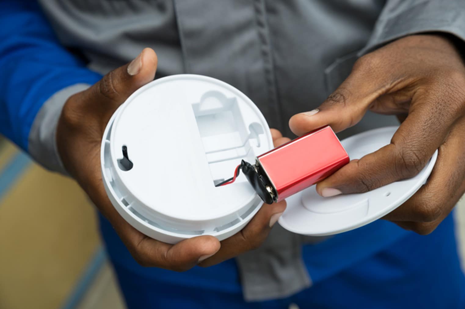 A man changes the batteries of a smoke detector inside his home. 