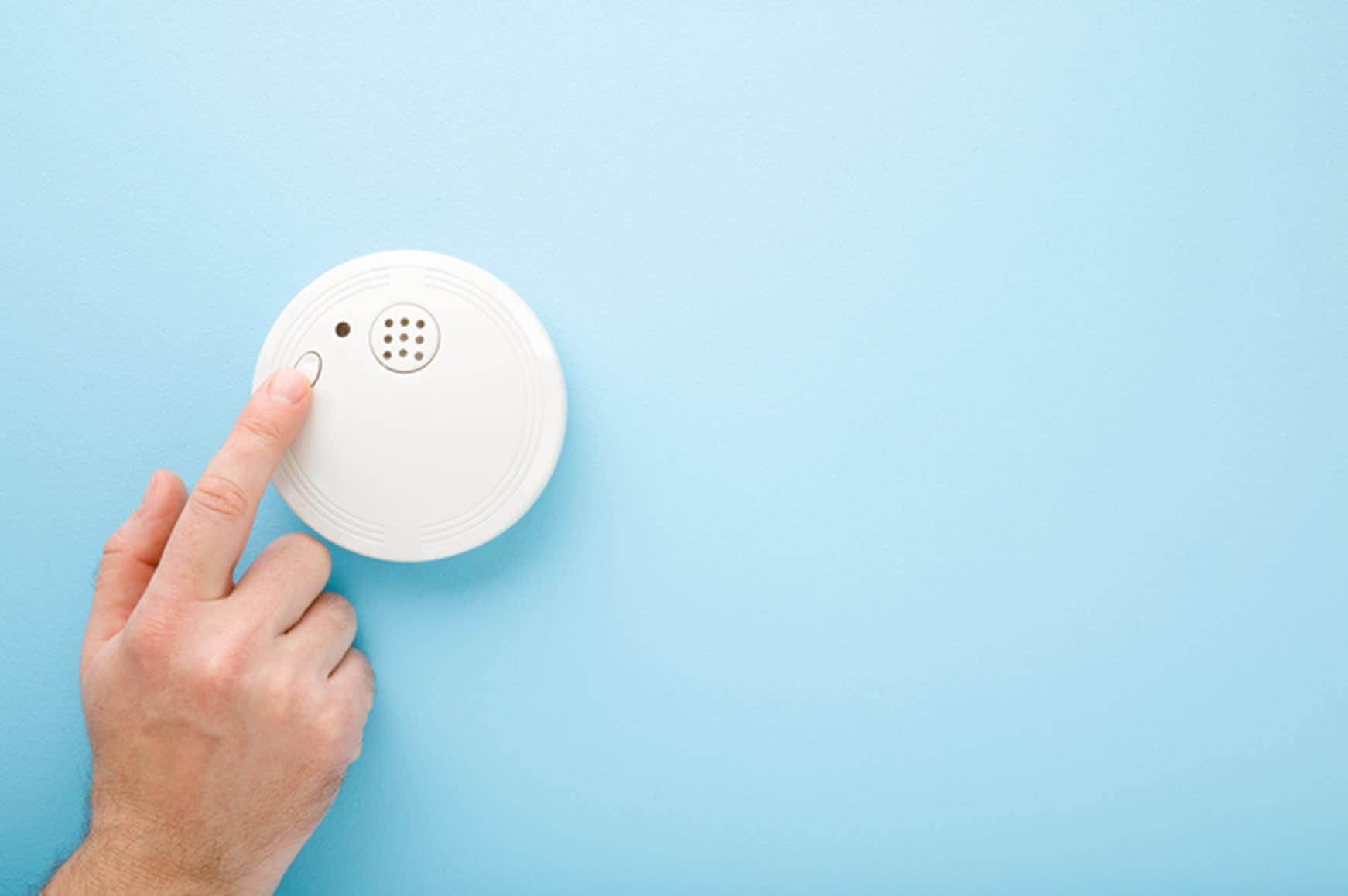 A person reaches to turn off the beeping smoke alarm on the wall in their home. 
