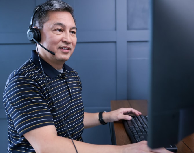 ADT customer service rep typing on his computer and troubleshooting with a customer on his headset 