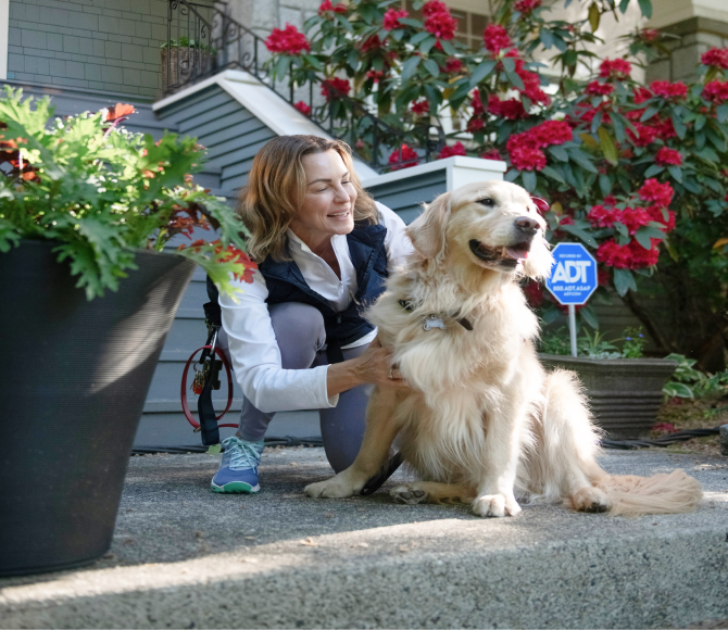 Woman kneeling next to her dog by an ADT sign