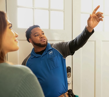 A female technician on a step ladder installs a smoke detector on the ceiling inside a modern home.