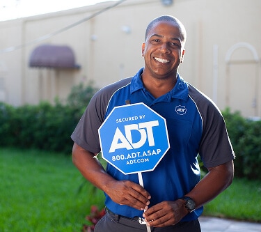A female technician on a step ladder installs a smoke detector on the ceiling inside a modern home.