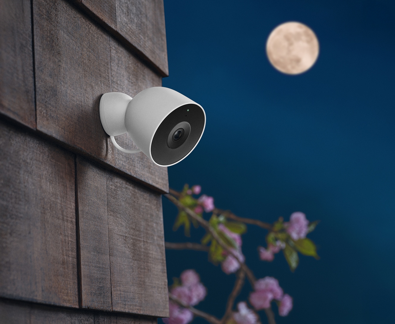 White outdoor security camera attached to a wooden exterior wall with a full moon visible in the night sky White outdoor security camera attached to a wooden exterior wall with a full moon visible in the night sky
