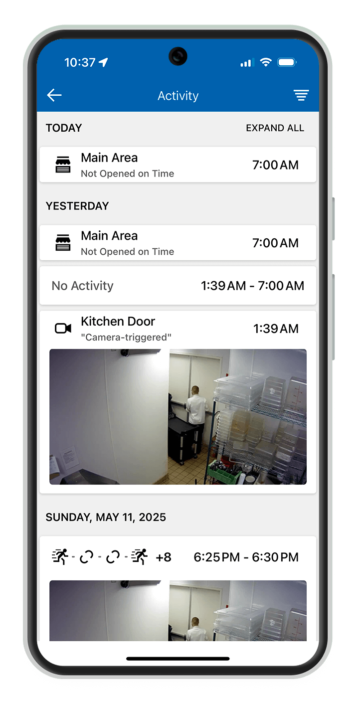 A smiling business owner in a yellow shirt and apron stands in a well-lit café, holding a tablet to manage operations.