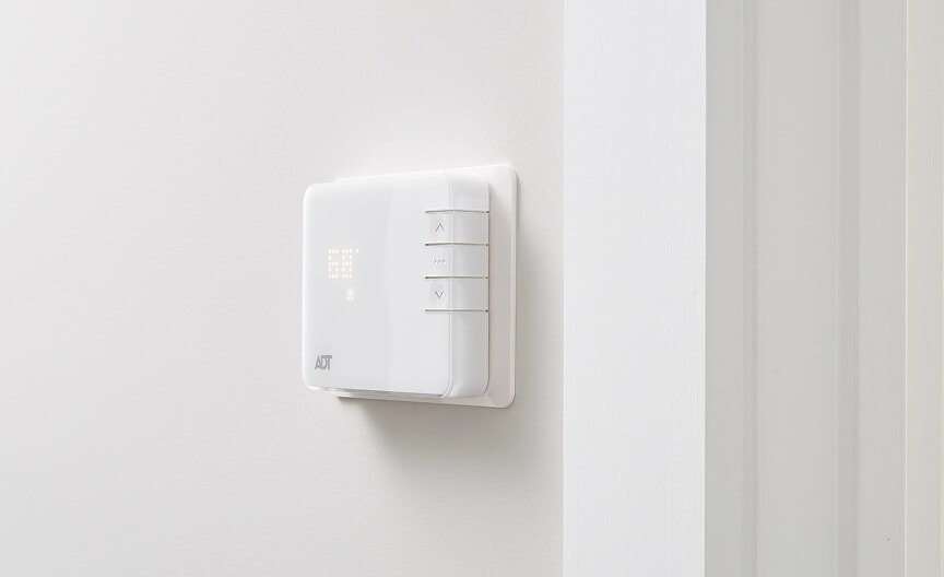 A wall-mounted ADT smart thermostat with simple controls and LED display for managing indoor climate.