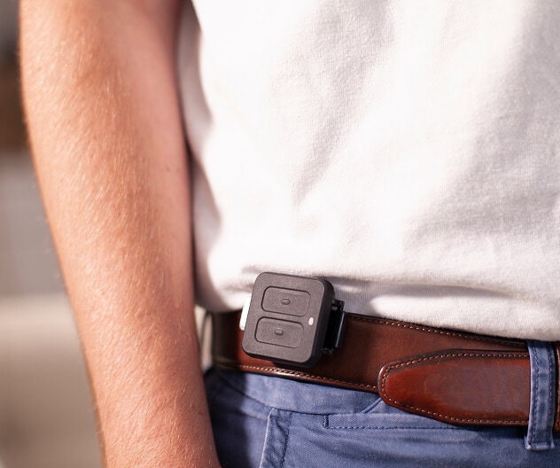 A portable ADT panic button device clipped onto the belt of a person wearing business-casual clothes.