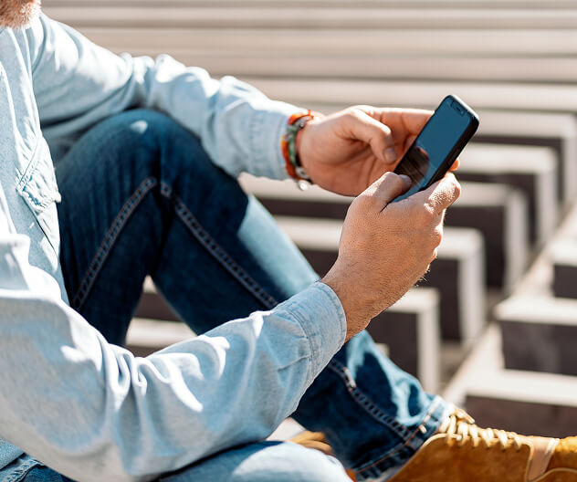 A person seated outdoors uses a smartphone, symbolizing remote control and monitoring of ADT business security systems.