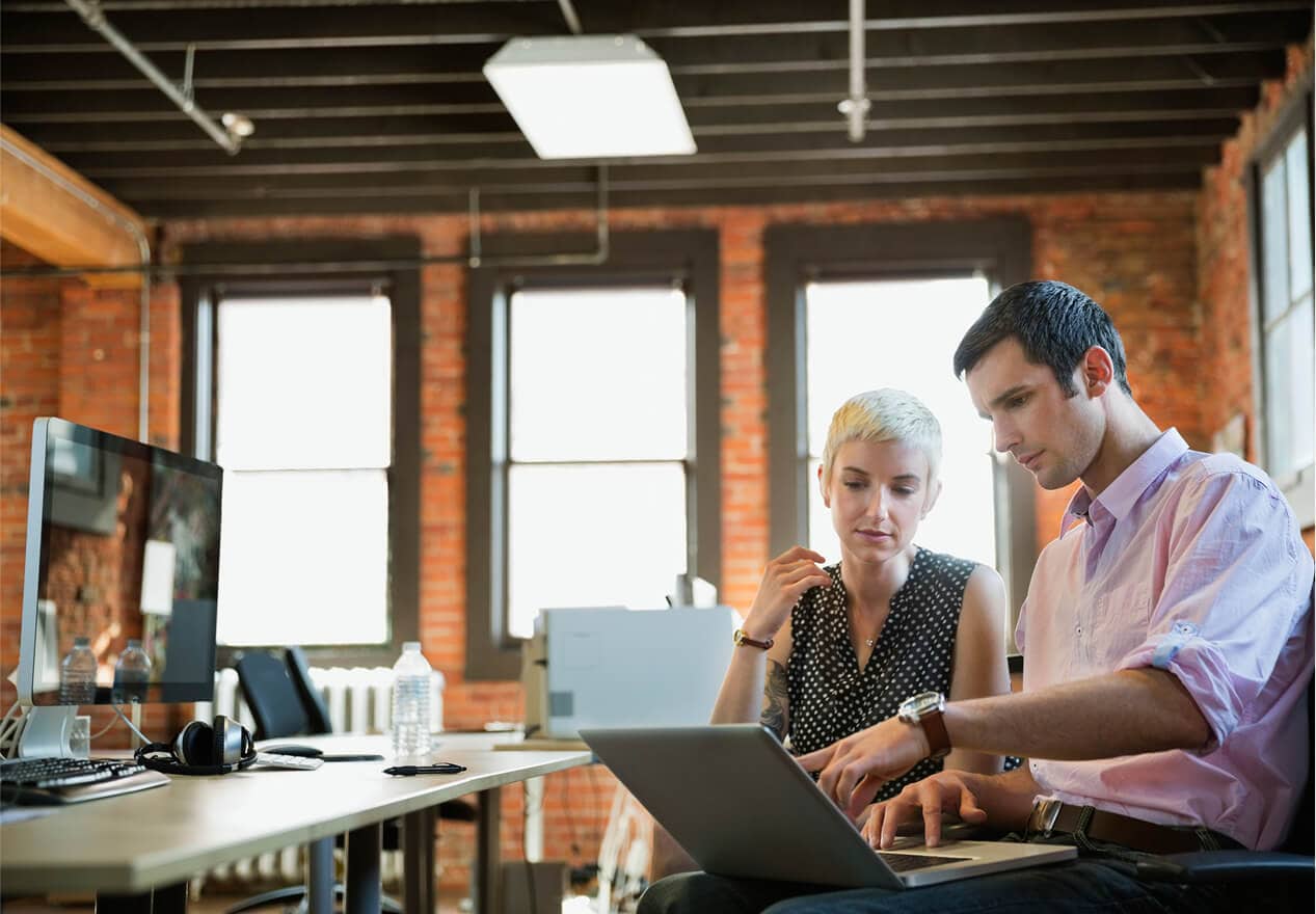 Two business owners in a modern office review information on a laptop, illustrating video business operations with ADT security.