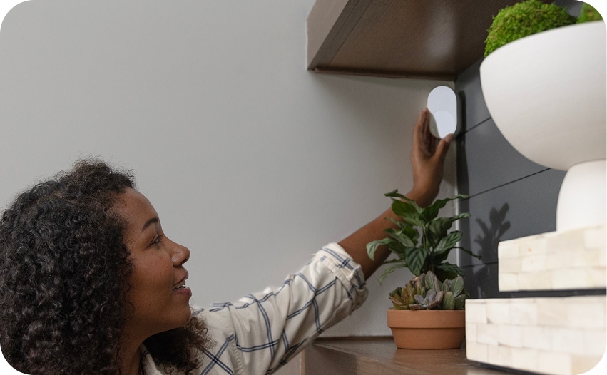 Woman installing a motion sensor on a wall at home