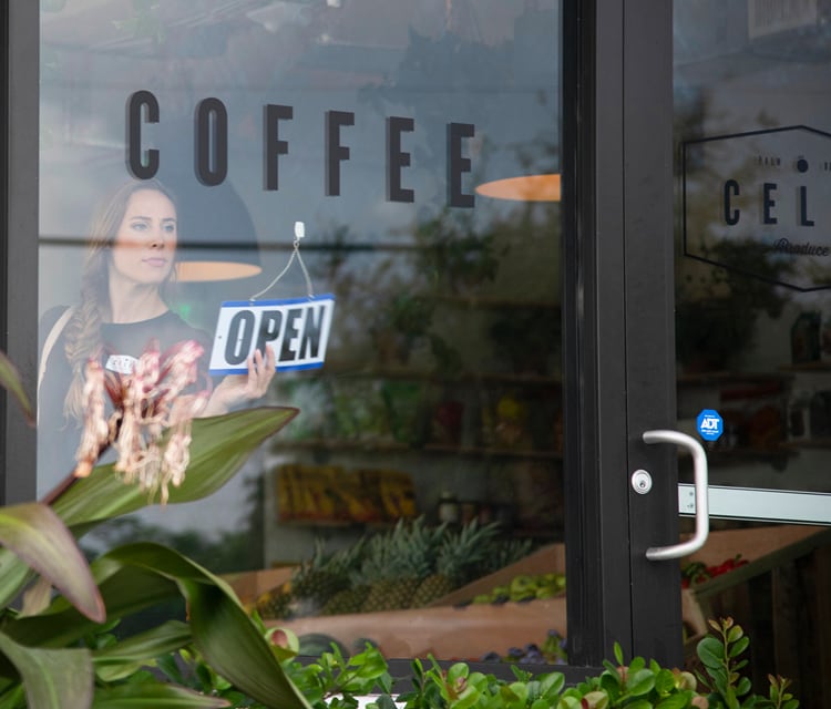 An employee places a “open” sign on the glass door of a café, which displays an ADT security sticker.