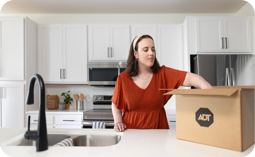 Person unpacking an ADT box on a kitchen counter, representing the components of a home security system.