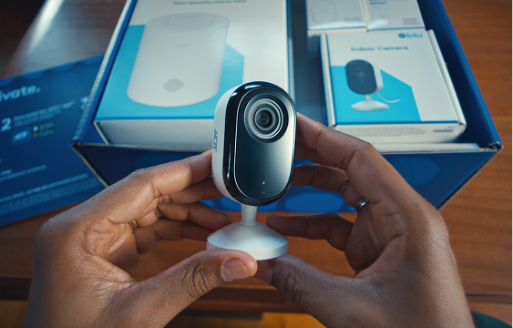 Hands holding a white indoor security camera over an open box of Blue by ADT components, labeled DIY Install.
