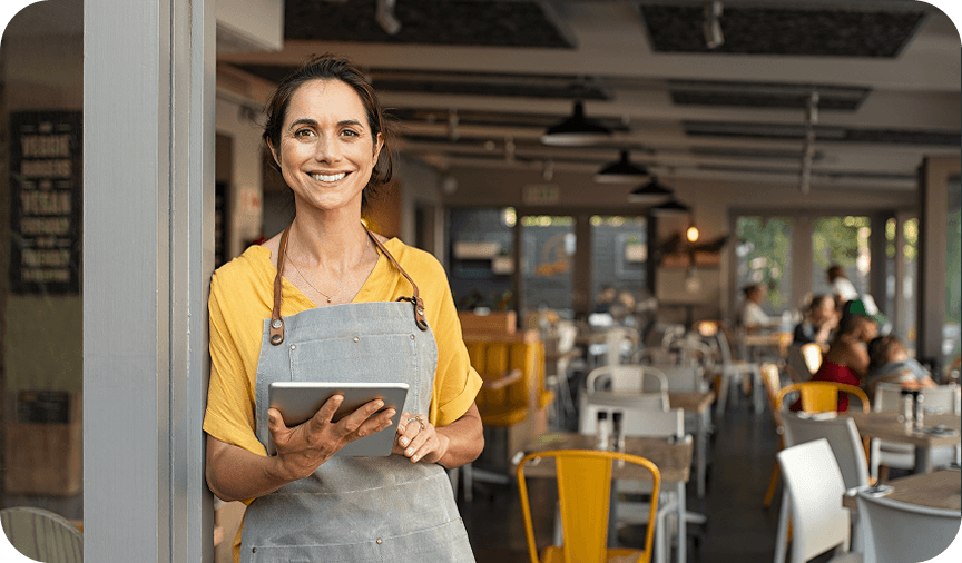 Smiling café owner in apron holding a tablet at the restaurant entrance.