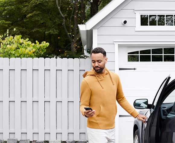 Man standing next to his car in the driveway logging into his My ADT account on the  app