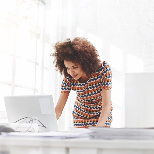 Woman in office leaning over laptop computer