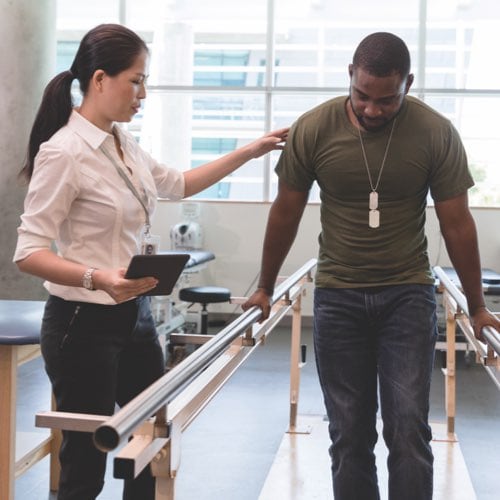 Therapist helping patient use parallel bars for walking exercise