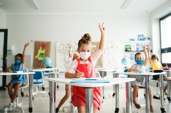Classroom of masked children raising hands