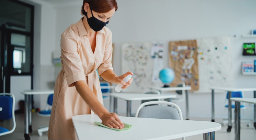 Masked teacher disinfecting school desks