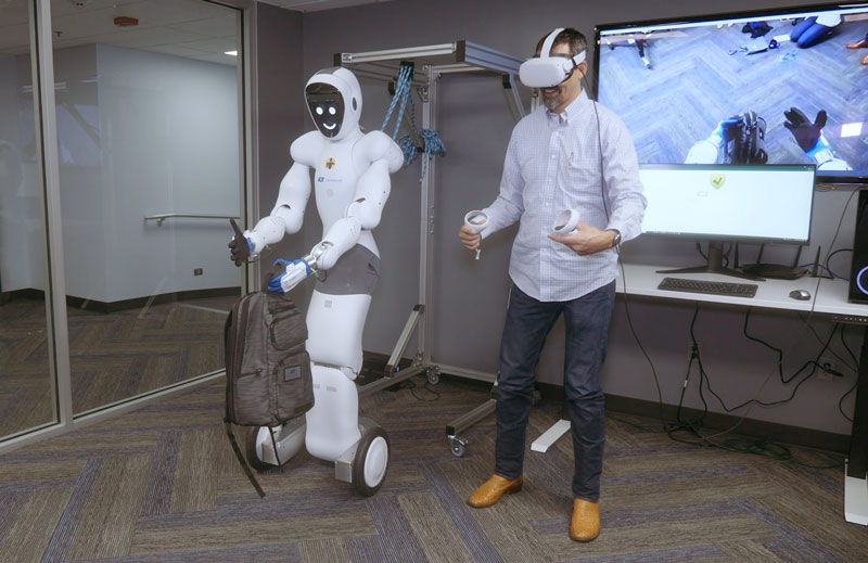 Man wearing VR goggles using humanoid robot to pick up backpack