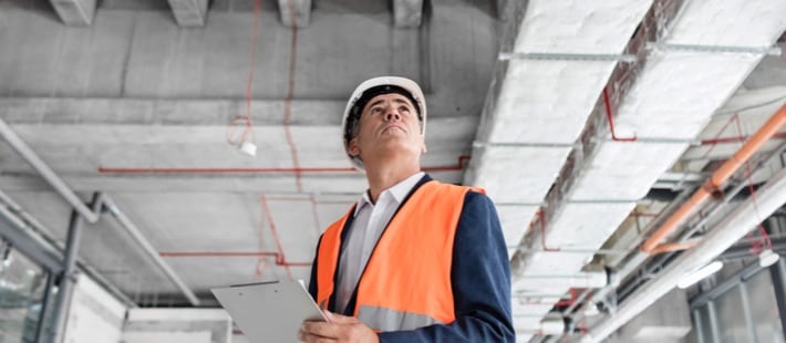 Man in hard hat and safety vest examining warehouse ceiling