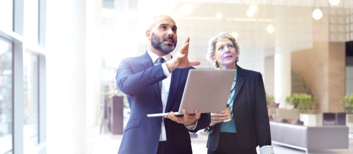 Man holding laptop showing woman a feature in an office environment