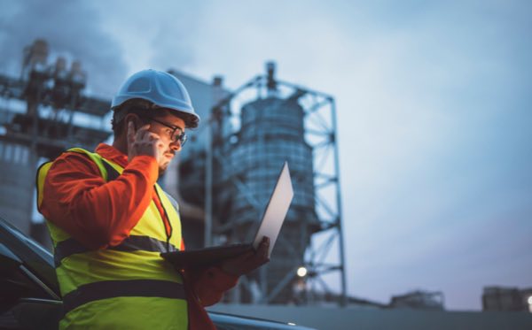 Power plant worker with phone and laptop outdoors at dusk