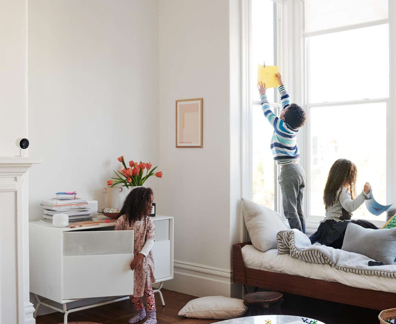 Siblings in their living room with a Google indoor camera on the fireplace