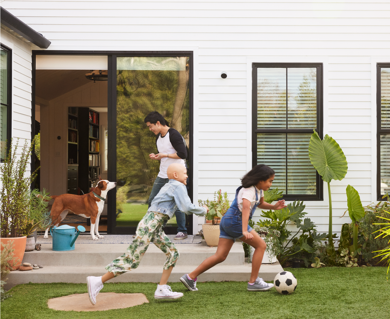 Kids playing soccer in backyard with Google Outdoor Camera installed on the house