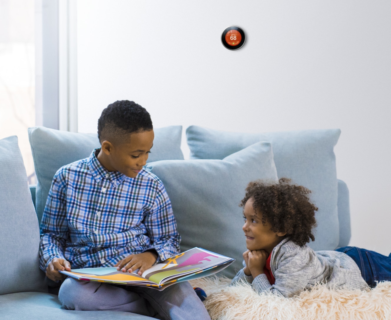 Brother and sister reading a book with Google Nest Learning Thermostat on the wall