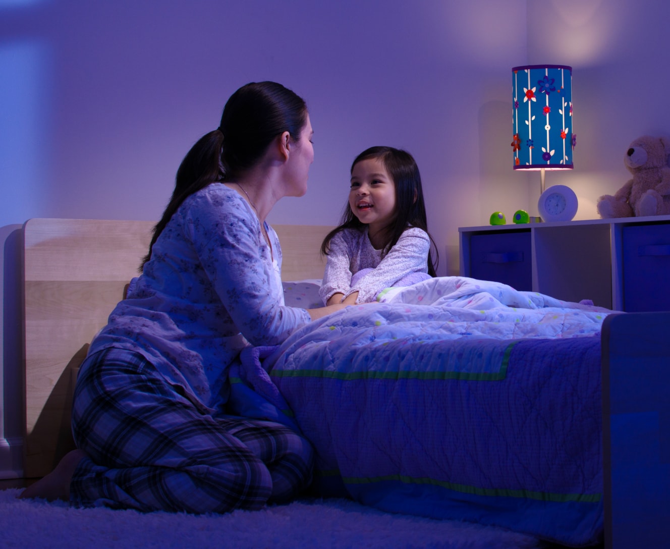 Mother tucking her child into bed while the Google Nest Learning Thermostat adjusts the bedtime scene