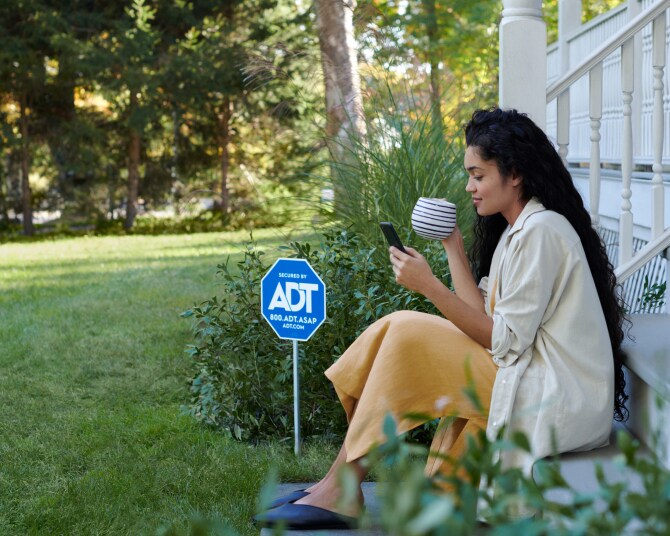 Woman sitting on her porch drinking coffee and looking at the ADT app on her phone