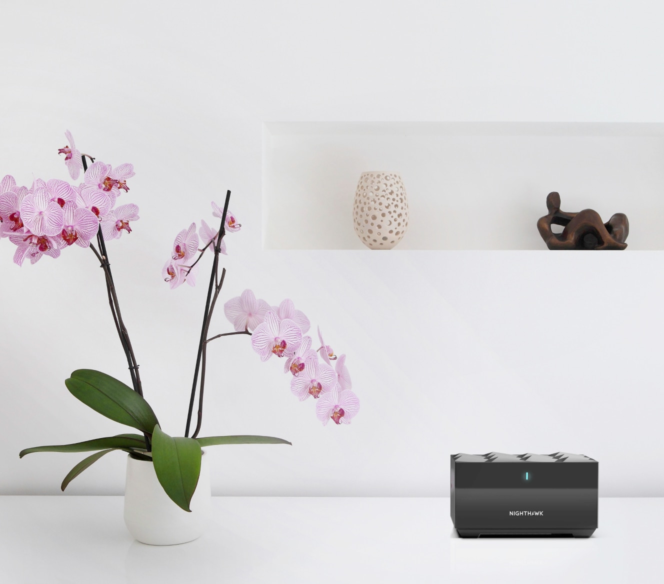 Netgear Mesh WiFi on a white table next to an orchid and vases Netgear Mesh WiFi on a white table next to an orchid and vases