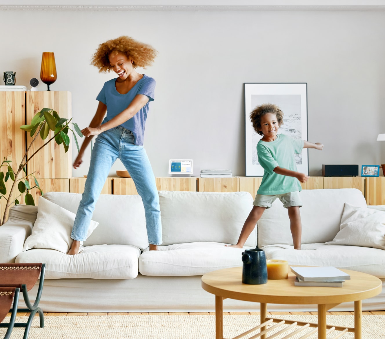 Google Nest Hub 2nd Gen on a shelf while a mother and son dance on their couch