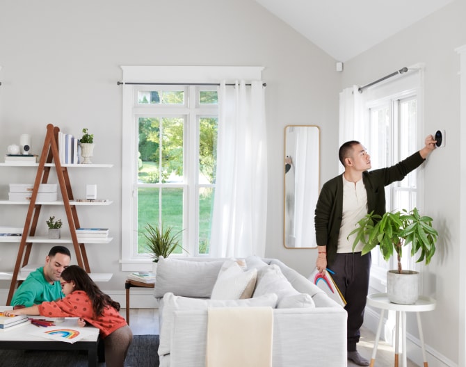 Family sitting in their living room while someone adjusts the Google Nest Cam (Indoor)