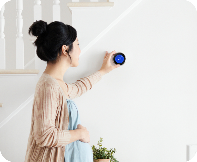 Pregnant women adjusting a Google Nest Learning Thermostat mounted on a wall
