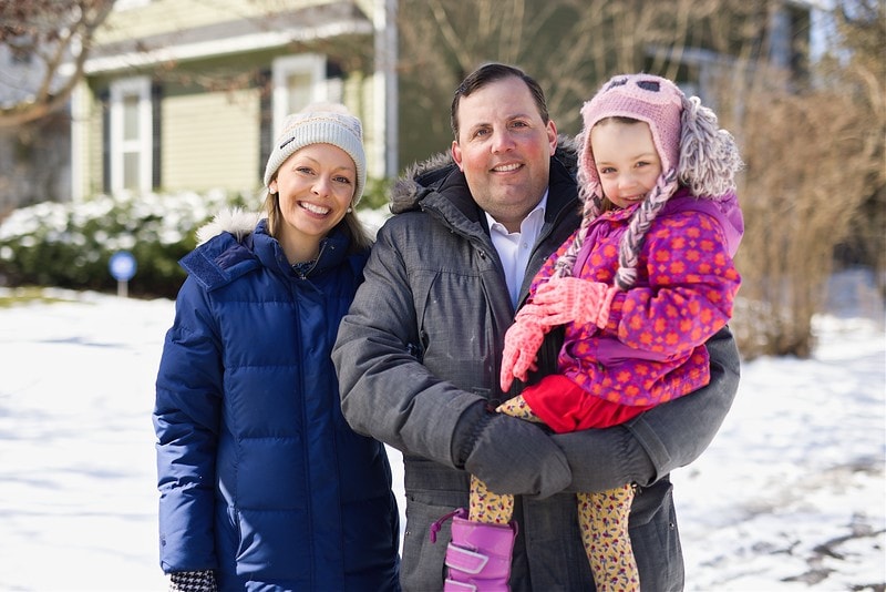 Image of three family members outside their home on a snowy day 